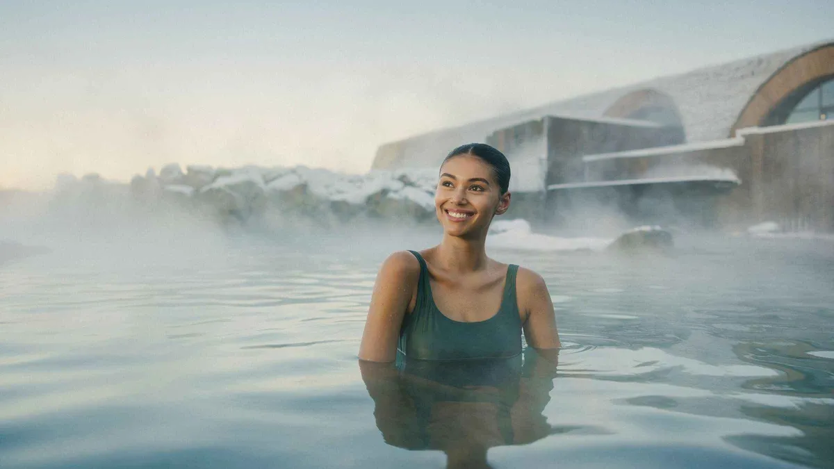 Bather in the milky geothermal water of Laugarás Lagoon in winter with snow on the surrounding lava rocks, South Iceland